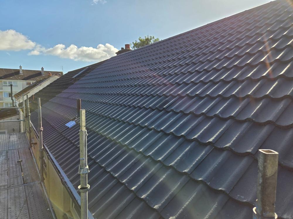 Low sun across a newly tiled grey roof, seen along the scaffold