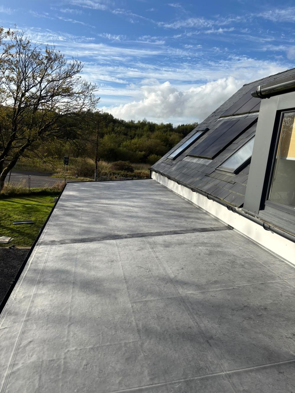 New grey EPDM rubber flat roof beside a modern clad dormer, blue sky