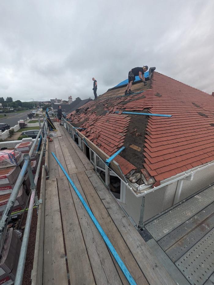 Roofers stripping old red tiles from a hip roof, scaffold all round