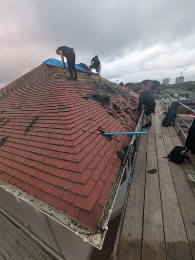 Team stripping old red tiles from a hip roof